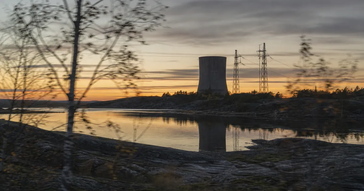 Industrilandskap vid kusten i skymning med kraftledningar och betongstrukturer speglat i stilla vatten