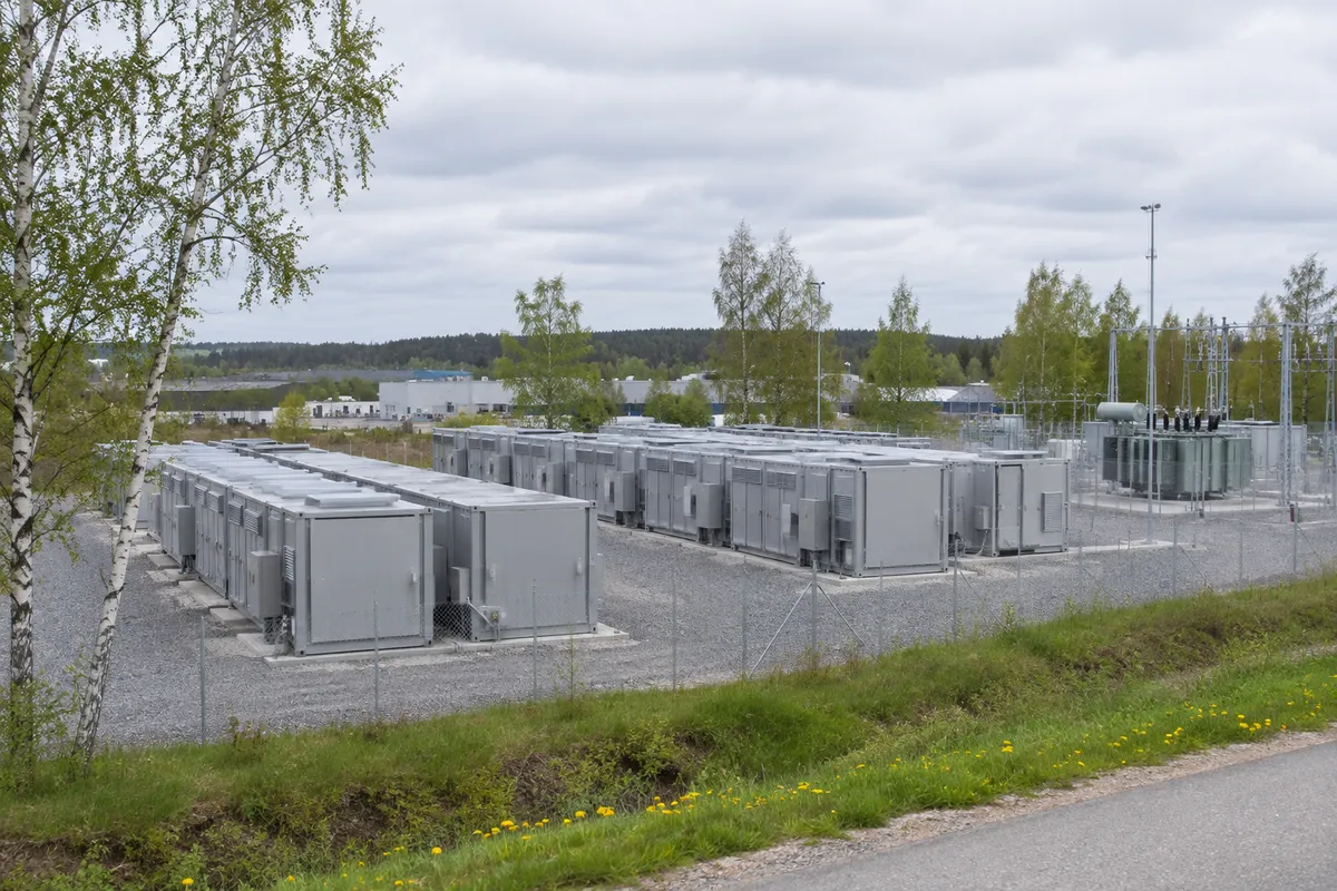 Batterilager i grå containrar på en inhägnad grusplan i utkanten av en svensk stad