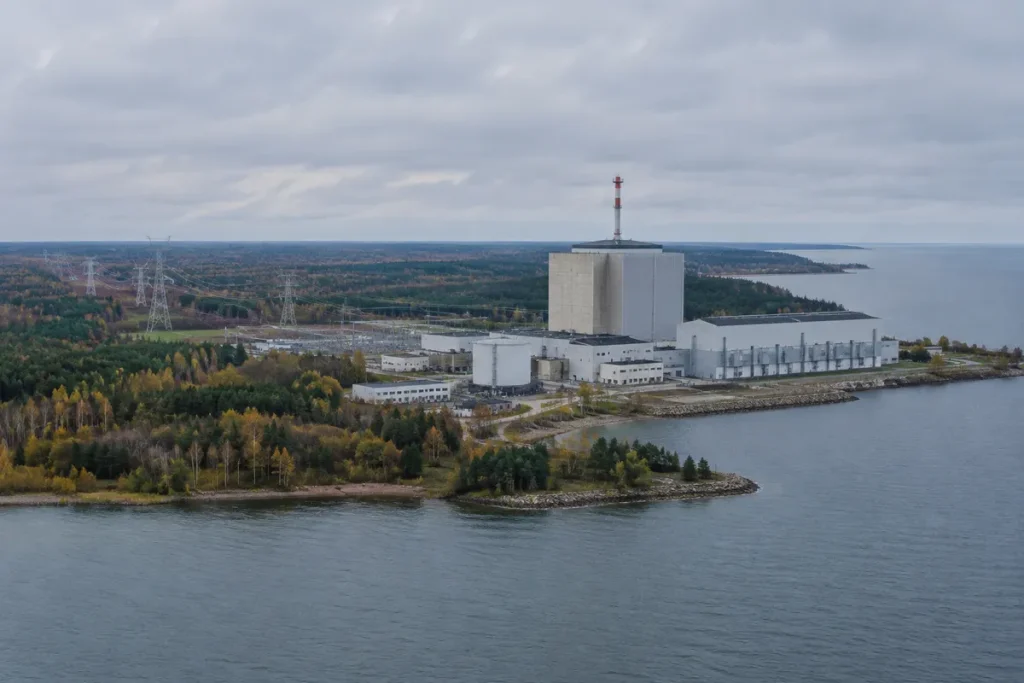 Kärnkraftverk med rektangulär reaktorbyggnad och turbinhall på en skogsklädd udde vid Östersjön